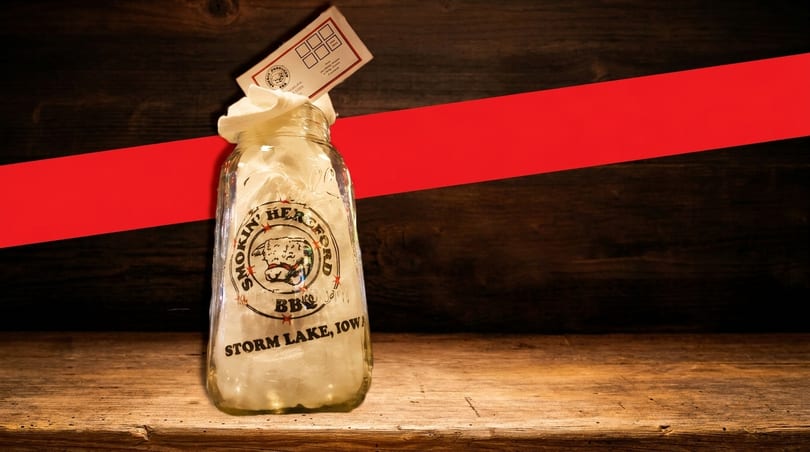 A Smokin' Hereford BBQ jar with a loyalty card on a wooden table with a red stripe.