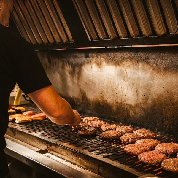Chef grilling numerous burger patties and chicken on a large, professional grill.