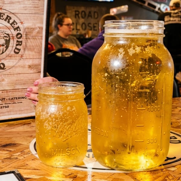 Two mason jars of beer on a wooden table with a menu in the background.