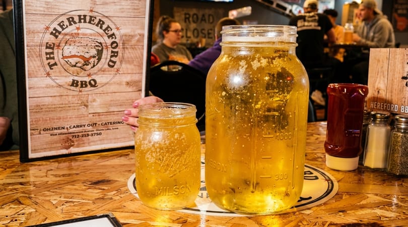 Two mason jars of beer on a wooden table with a menu in the background.