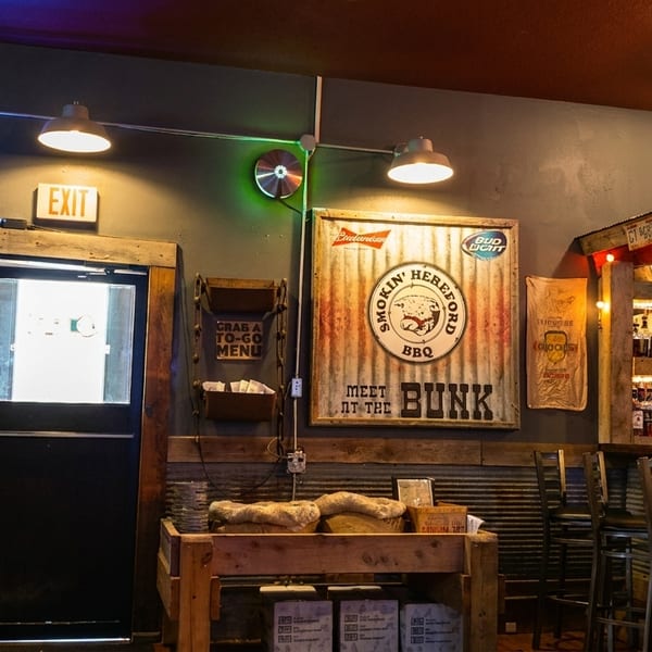 Rustic interior of a BBQ restaurant with a bar and Smokin' Hereford BBQ sign.