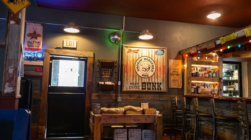 Rustic interior of a BBQ restaurant with a bar and Smokin' Hereford BBQ sign.